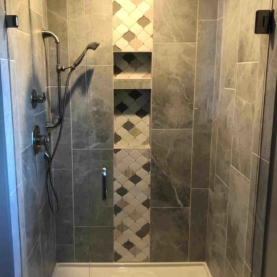 AFTER The new master bathroom shower includes a waterfall tile accent, a built-in niche with two shelves, clear glass pivot shower door, and a handheld shower arm along with a fixed shower head.