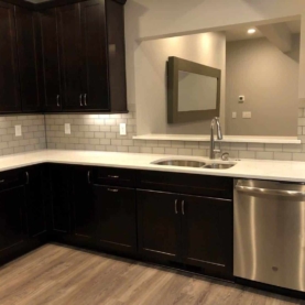 AFTER The kitchen is complete with quartz countertops, beautiful dark cabinets, glass subway tile, and LVP flooring. The feeling of openness and unity was created by including a pass through, which allows the kitchen and living room to be connected without sacrificing wall space for upper and lower cabinets. The matching bar top creates a convenient place for drinks and appetizers when the guests arrive.
